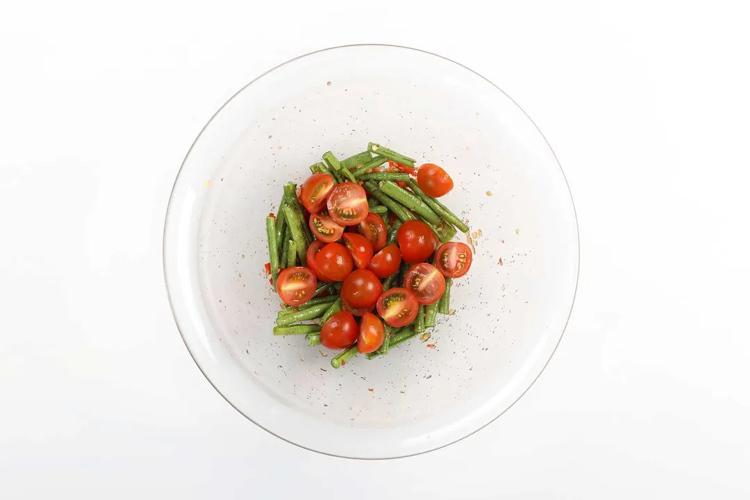 A large glass bowl containing long beans and halved tomatoes