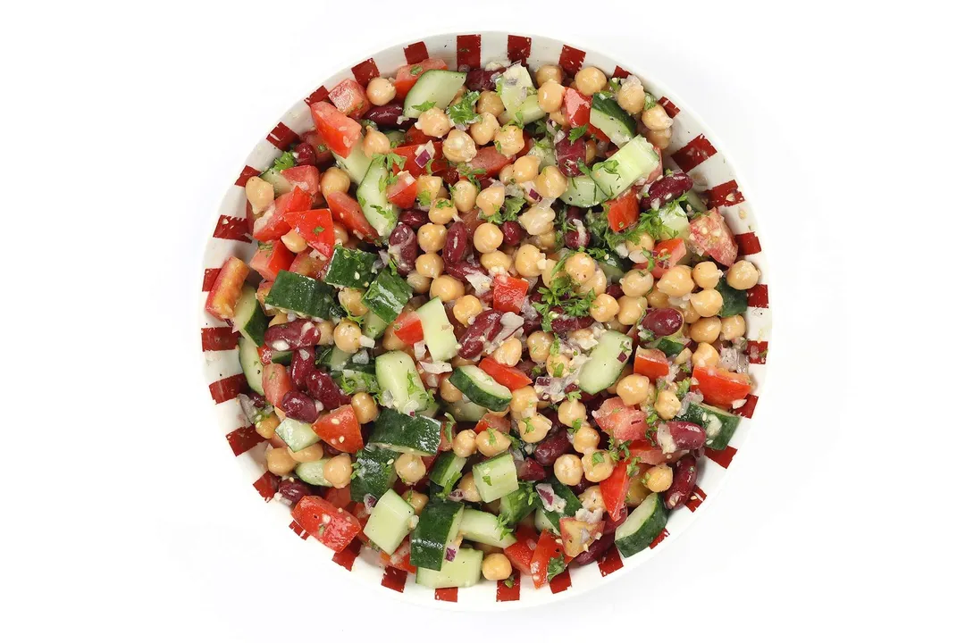 A colorful plate filled with chickpeas, diced cucumbers, diced tomatoes, and diced red onion.
