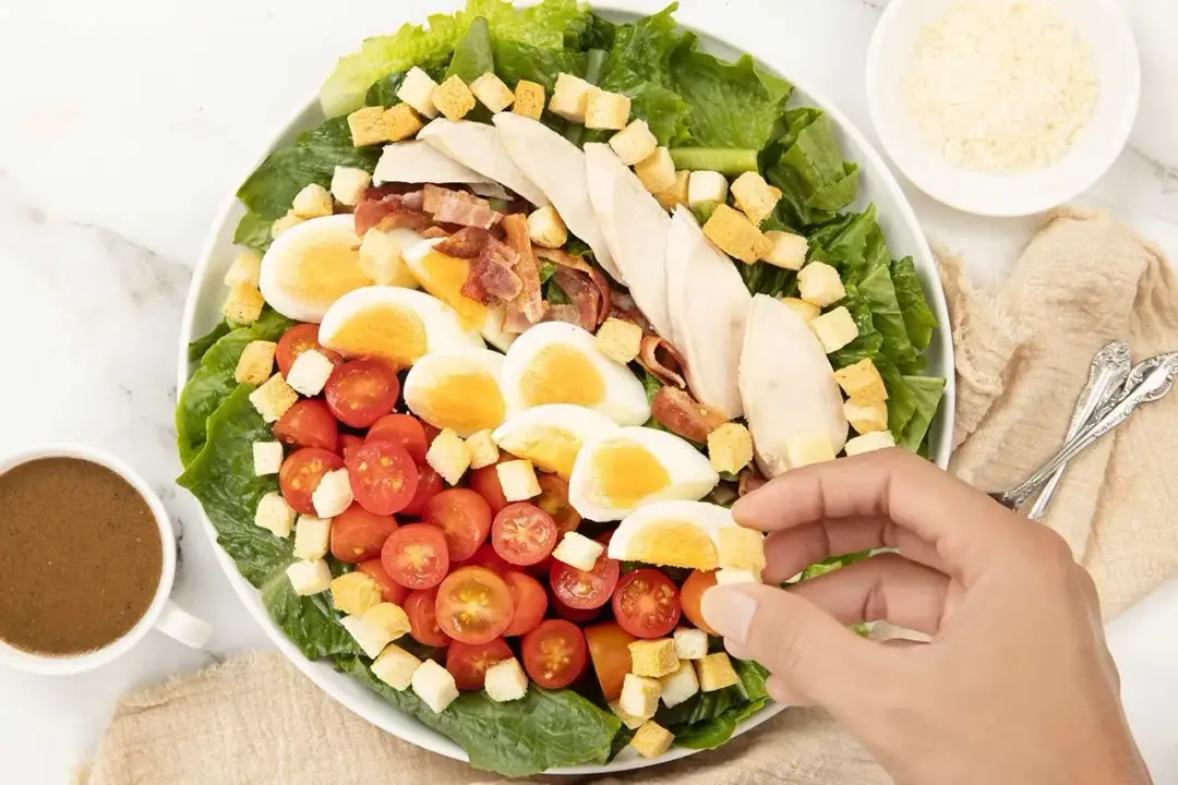 a platter of Caesar salad with croutons, boiled eggs, sliced chicken, and cherry tomatoes