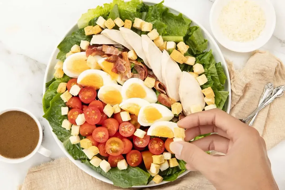 a platter of Caesar salad with croutons, boiled eggs, sliced chicken, and cherry tomatoes