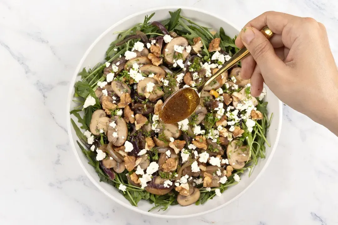 A bowl of mushroom salad with sliced mushrooms, chopped herbs, and dressing on top.