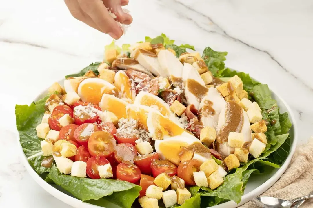 A plate of Caesar salad with lettuce, croutons, eggs, cherry tomatoes, and dressing