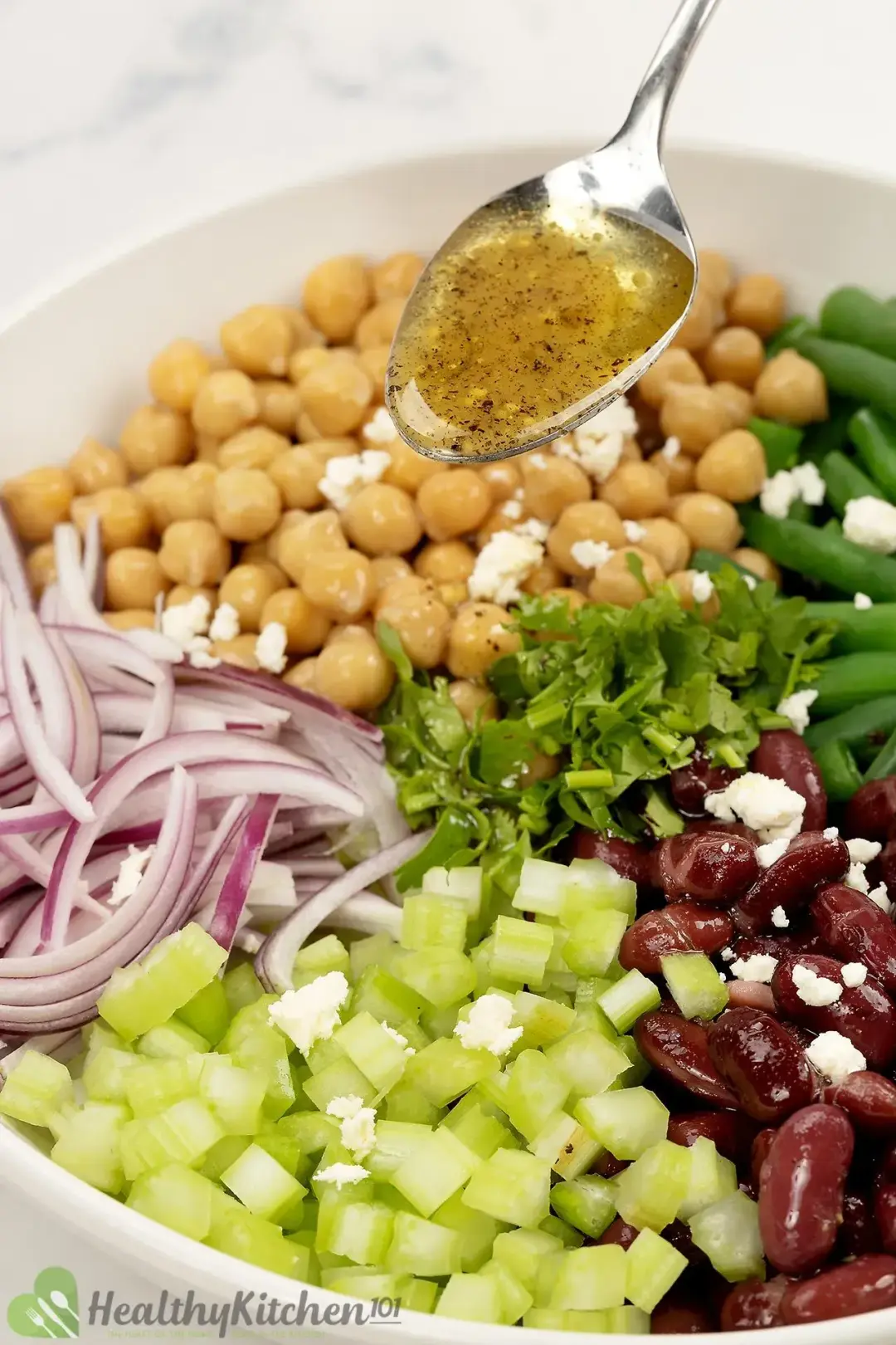 A bowl of three-bean salad with dressing, garnished with fresh herbs.