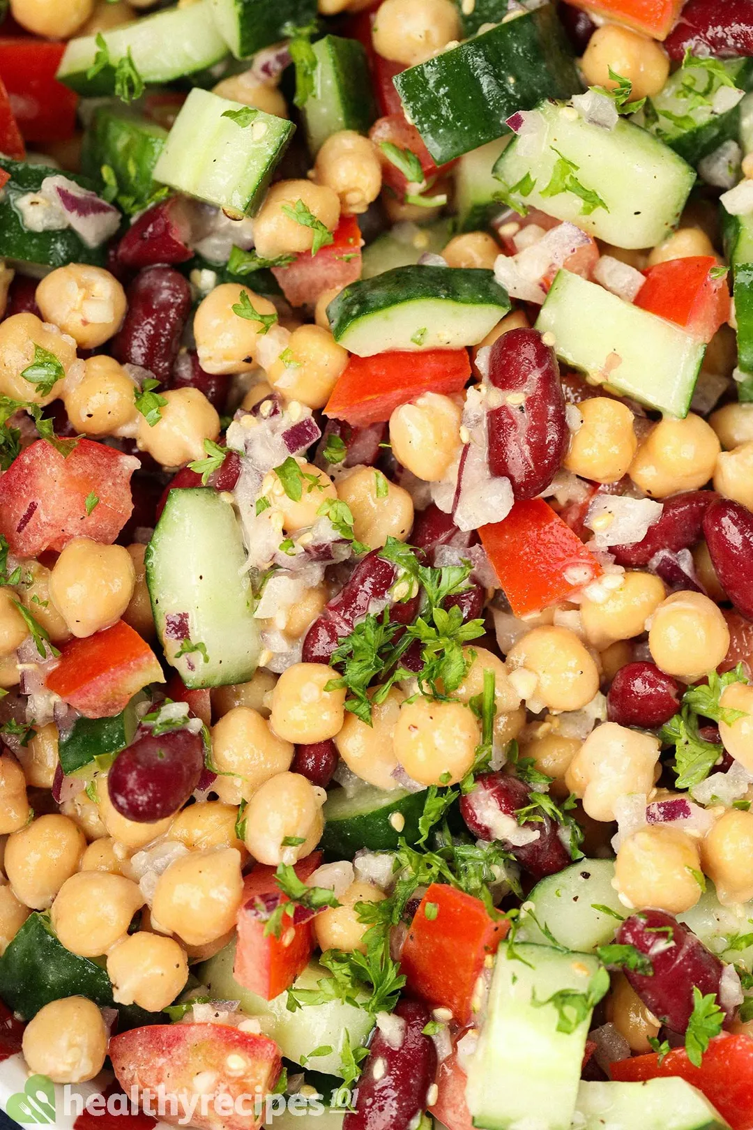 A close-up shot of vegan chickpea salad, showcasing a colorful mixture of chickpeas, coarsley-diced cucumbers, coarsley-diced tomatoes, chopped parsley, and diced red onion. 