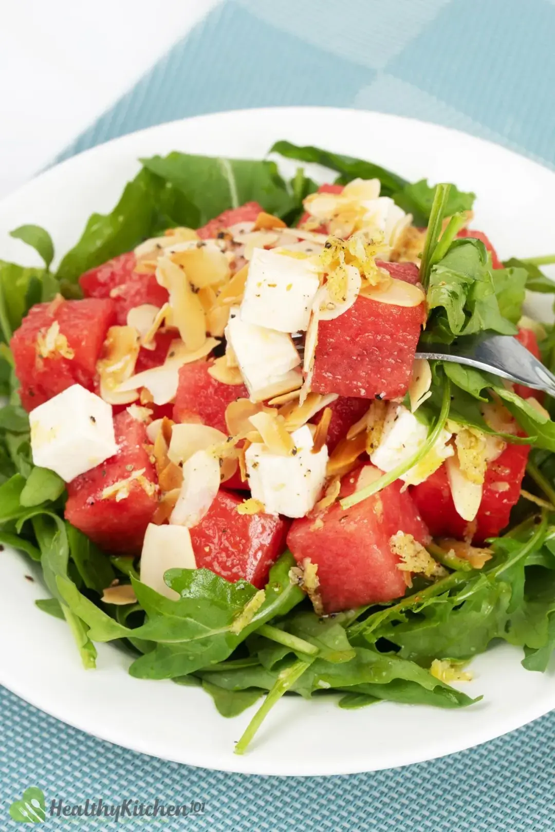 A plate of watermelon arugula salad, topped with cubed feta cheese and shaved almonds