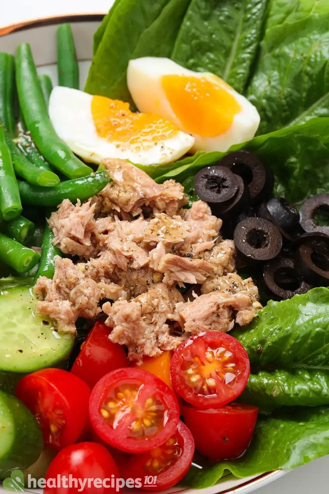 A bowl of Nicoise salad with boiled eggs, green beans, cherry tomatoes, olives, and tuna on a bed of lettuce.