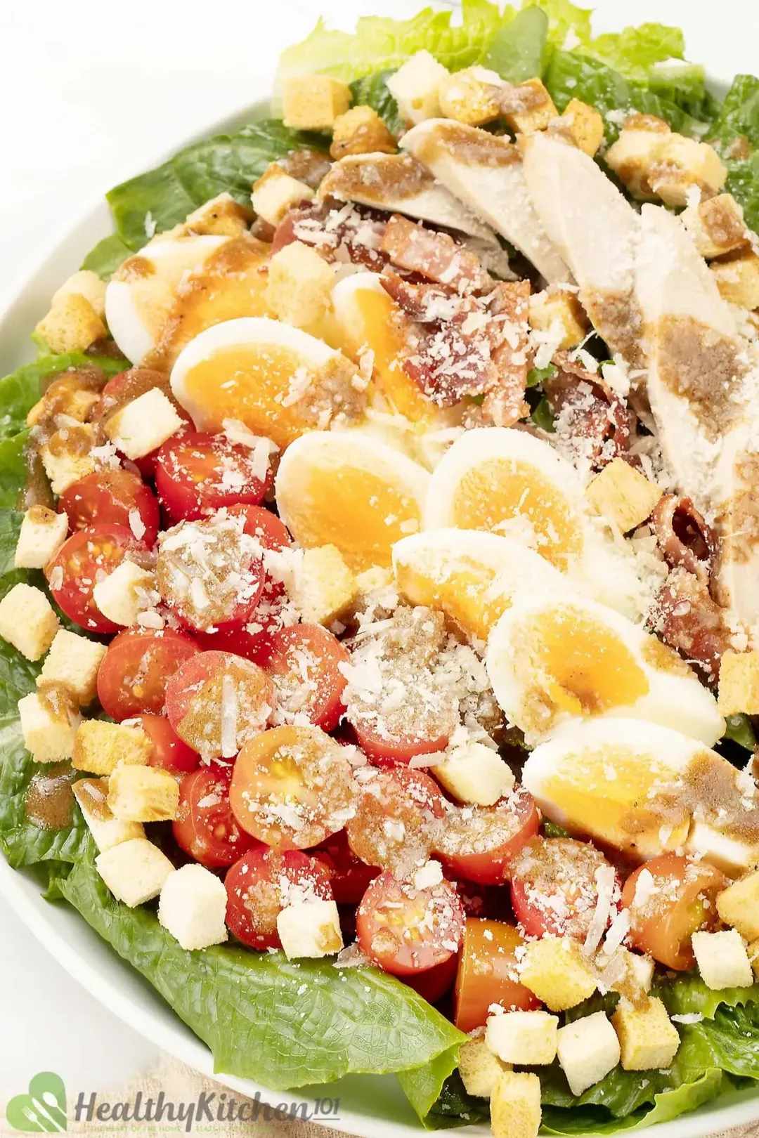 A variety of Caesar salad ingredients on a platter: including grilled chicken, cherry tomatoes, boiled eggs, lettuce