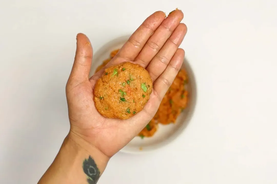 A close-up picture of an airfryer salmon patty in the palm of a hand in the background of a bowl of other salmon patties.