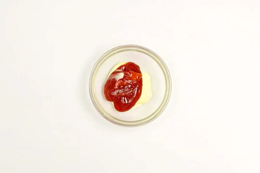 A small glass bowl with some mayonnaise and ketchup in it.
