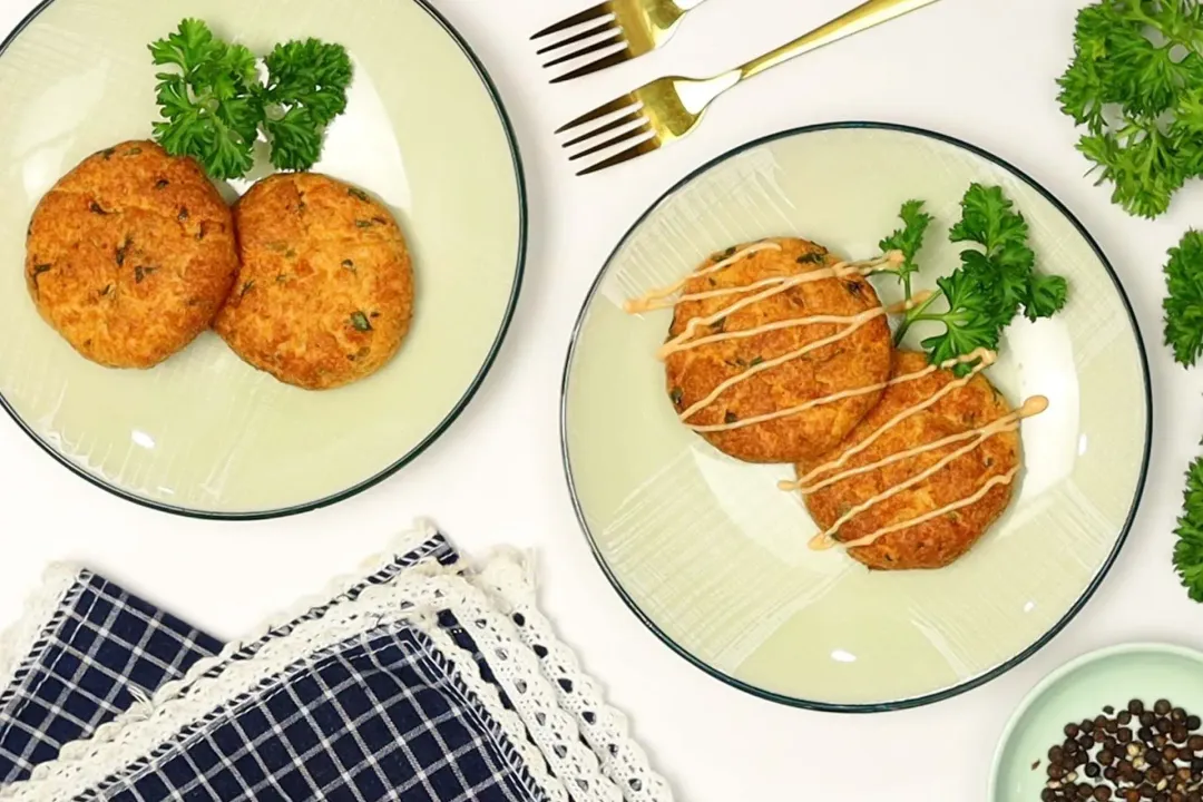 Two plates of air fryer salmon patties drizzled with sauce on top and garnished with some parsley.