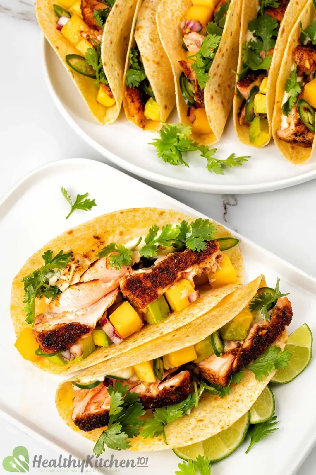 Two white plates of some blackened salmon tortillas, decorated with fresh parsley and lime slices.