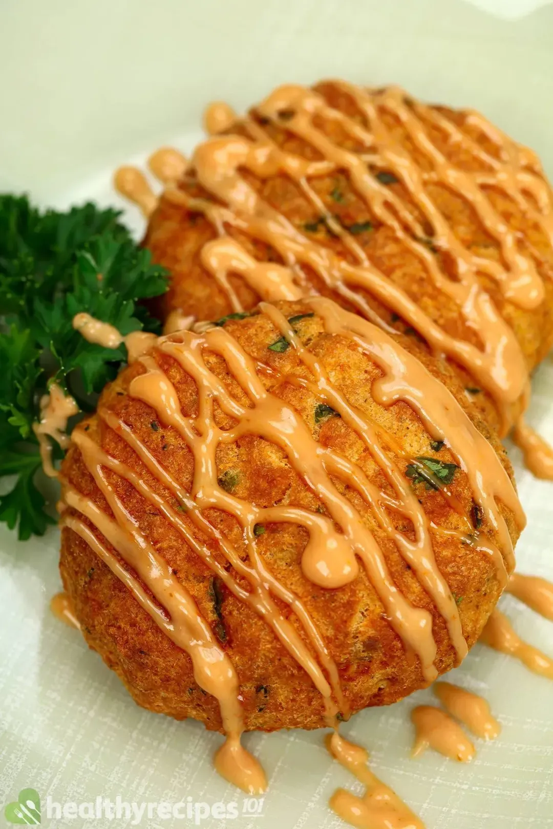 A close up picture of two air fryer salmon patties drizzled with sauce on top and garnished with some parsley.