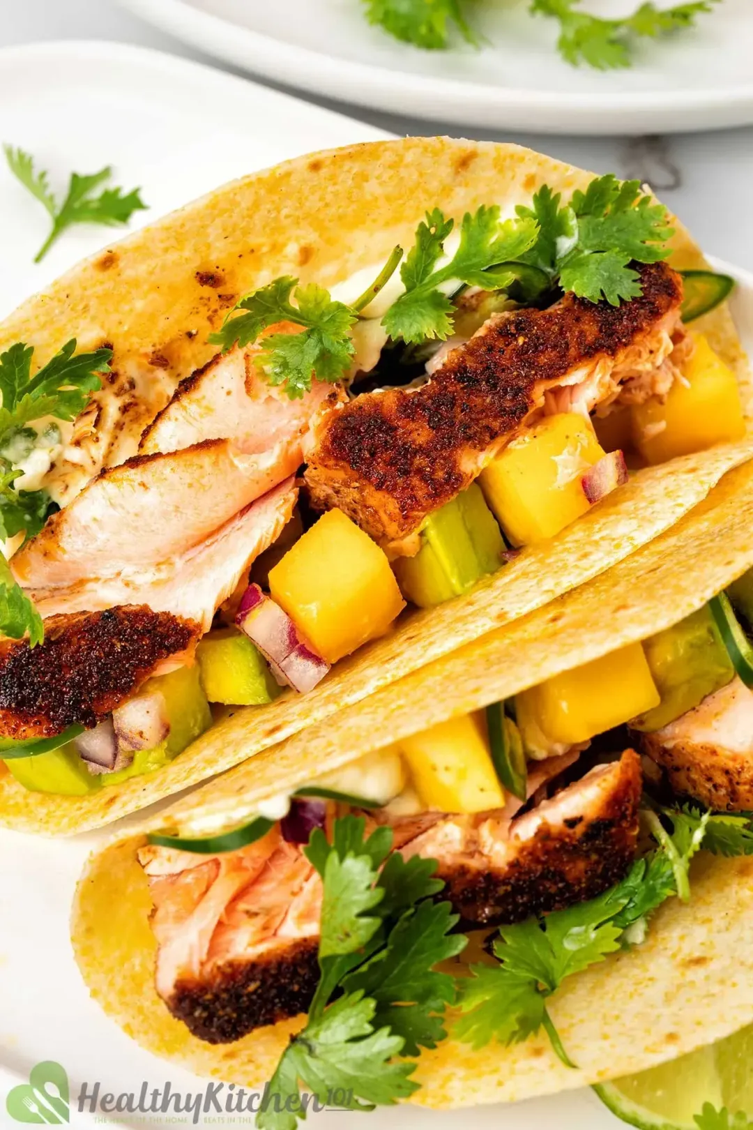 A close up picture of two blackened salmon tacos on a white plate decorated with some parsley on top.