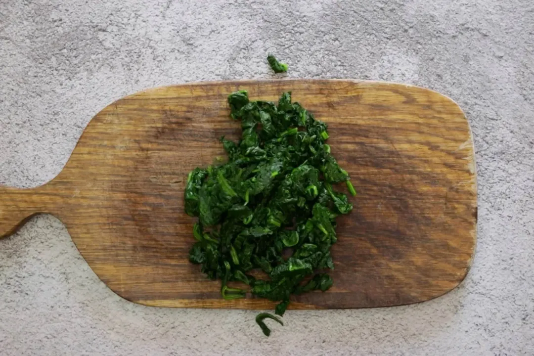 A chopping board with a bunch of cooked spinach