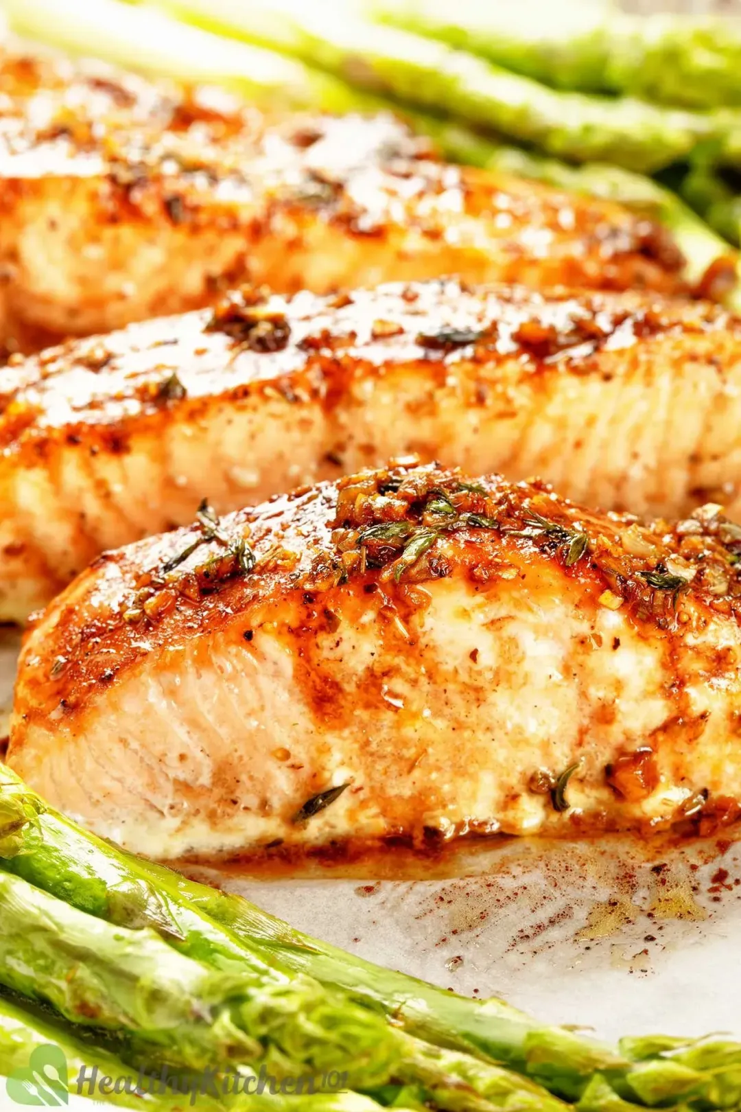 Three cooked salmon fillet surrounded by asparagus on baking tray