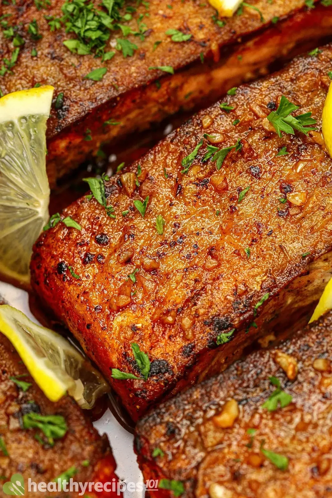 Golden brown pan-seared salmon fillets with lemon slices and some chopped parsley on top.