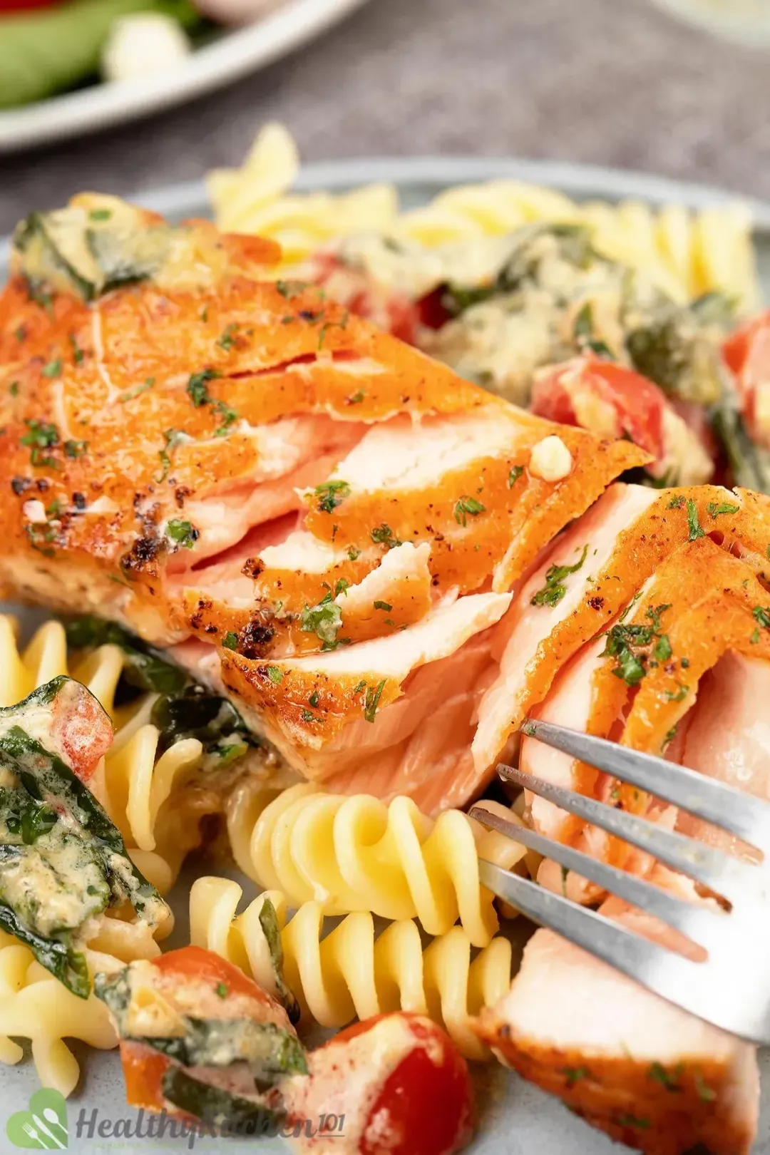 A closeup shot of cooked and flaked salmon atop creamed spinach, cherry tomatoes, and cooked rotini