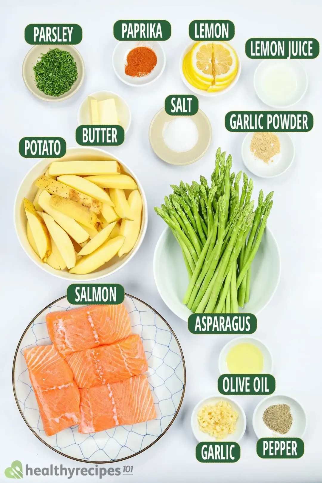 Plates containing salmon fillets, asparagus stalks, potato wedges, lemon slices, chopped parsley, and various spices