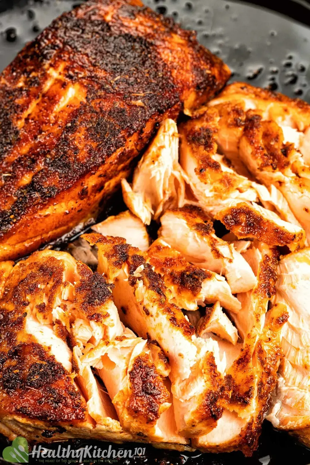 A close up picture of a blackened salmon fillet and a teared-up blackened salmon fillet in a black skillet.