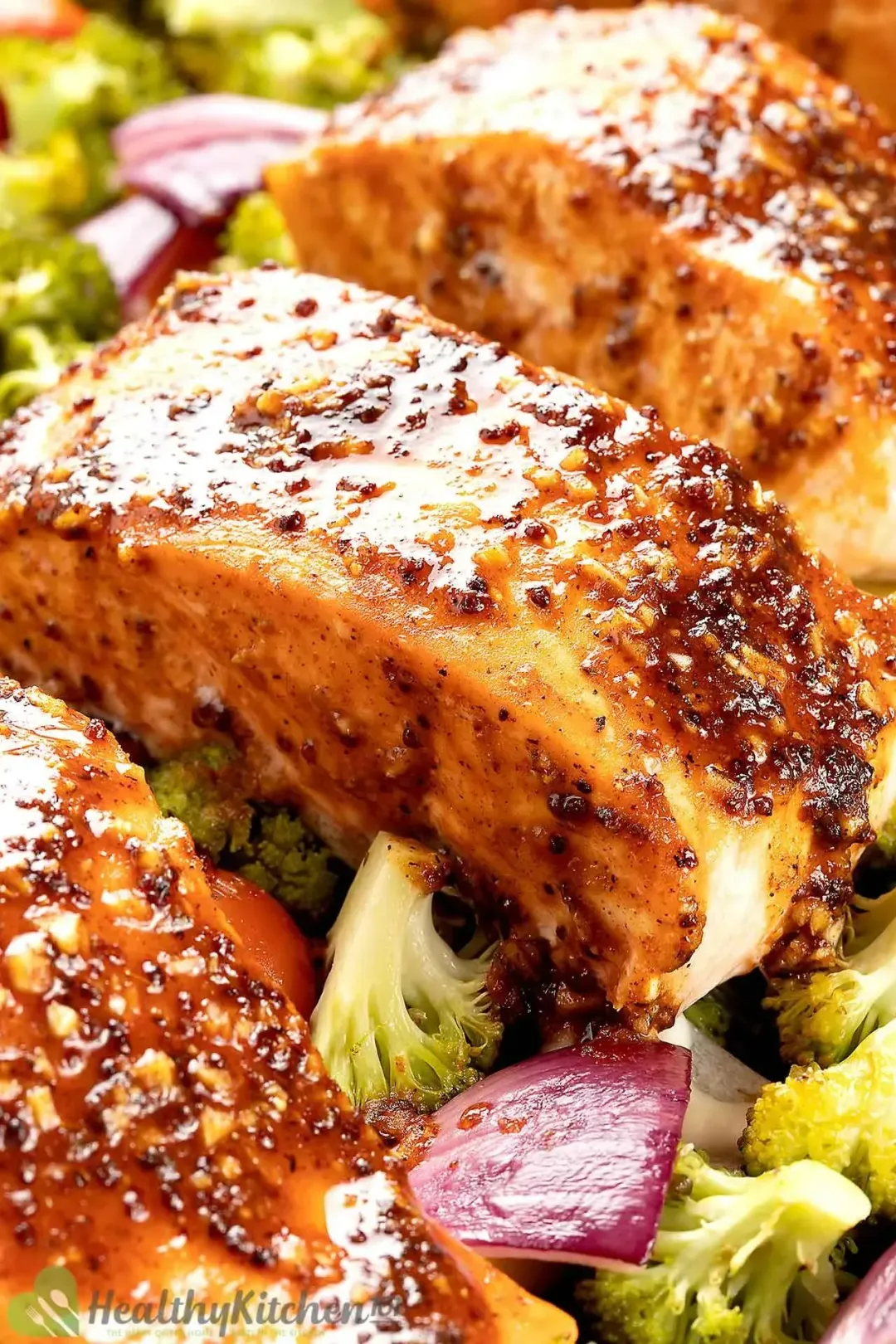 A close-up shot of salmon fillets covered in a glossy brown sauce and surrounded by broccoli florets and red onion pieces