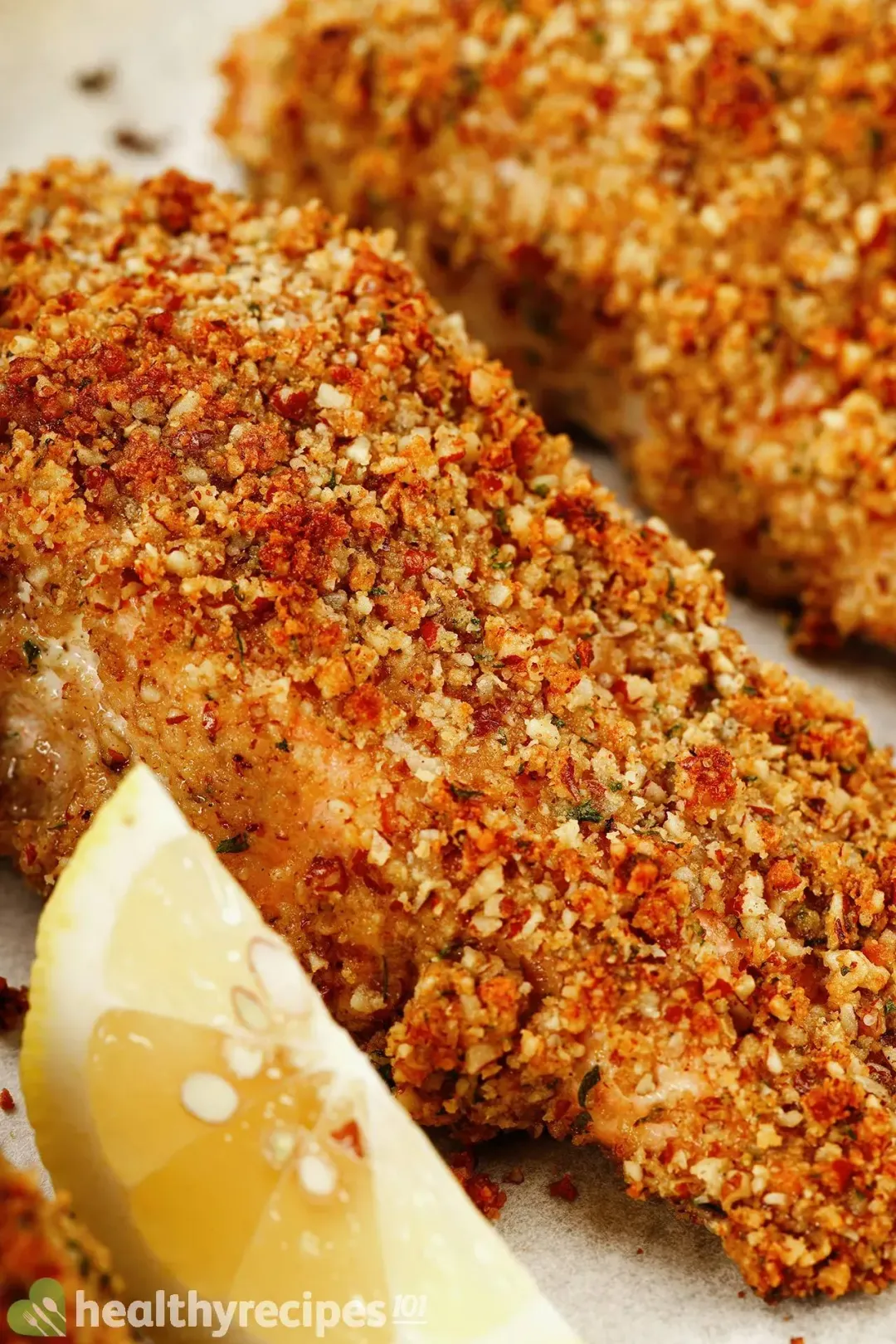 A close-up view of the outer surface of baked pecan-crusted salmon filets, with a lemon slice on the side.