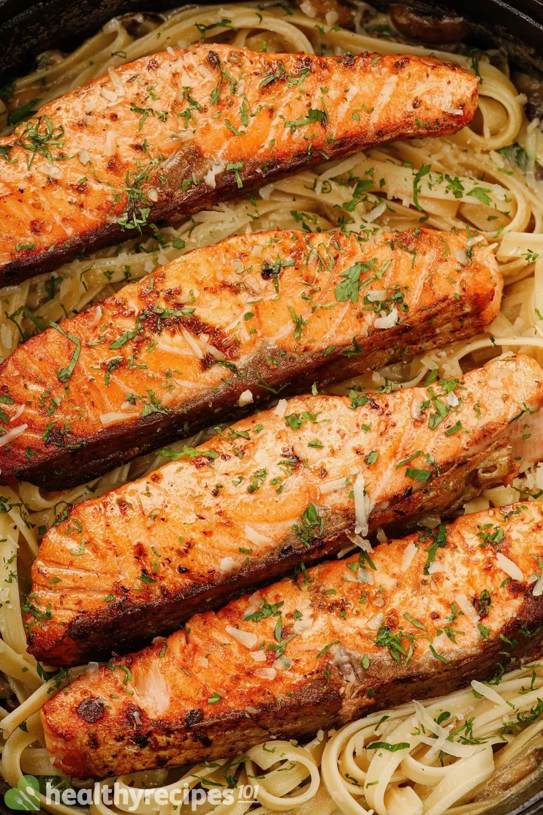 A close-up shot of four bright orange cooked salmon fillets sprinkled with chopped parsley and laid on a bed of fettuccine pasta