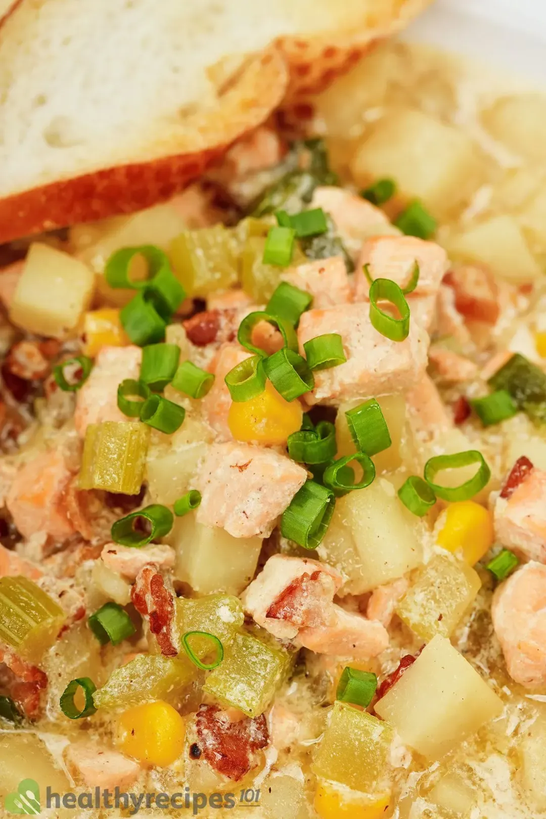 A close-up picture of chicken chowder topped with baguette slices and chopped scallions