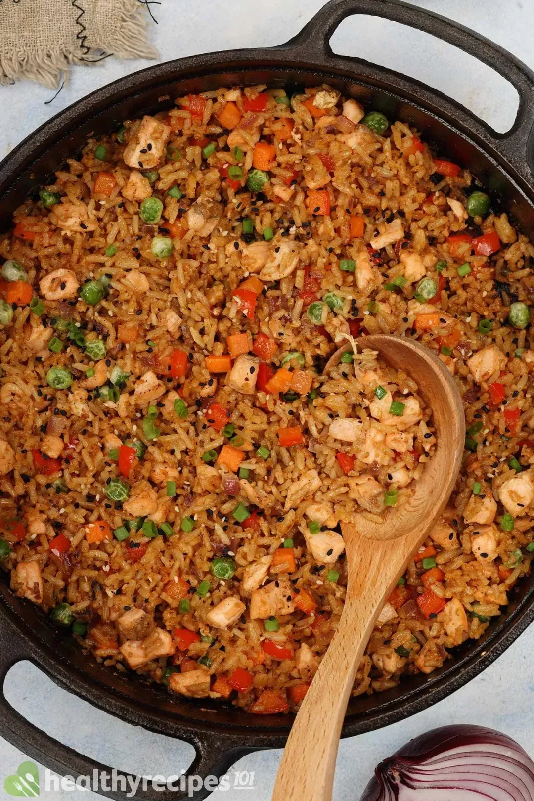 A large skillet of chunked salmon, pepper, carrot, peas, and onion fried with rice, with a wooden spoon dunked in