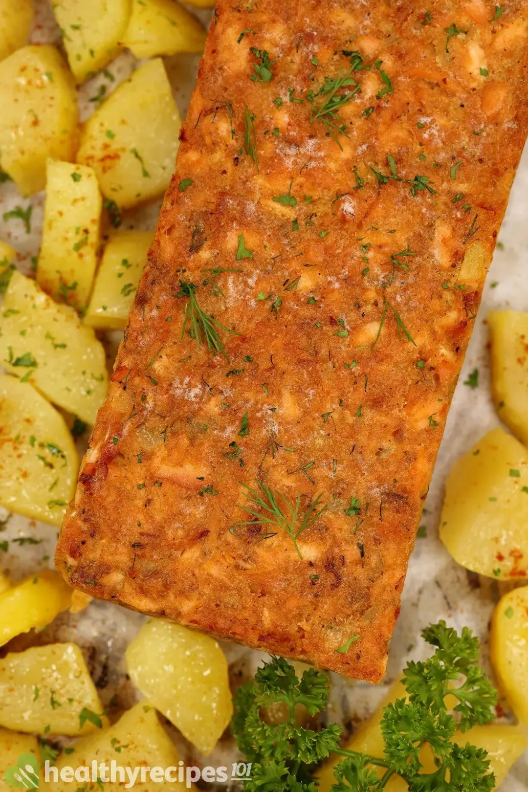 A high-angle shot of a salmon cake laid on parchment paper along with small potato cubes and a fresh parsley