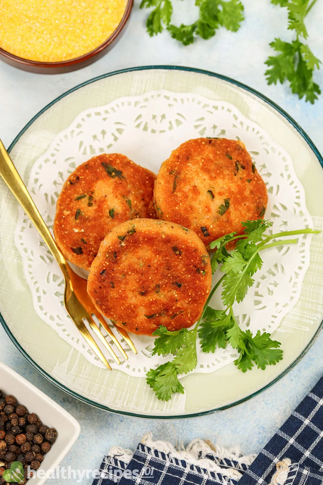 three salmon patties on a plate garnished with a fork and a bowl of cornmeal