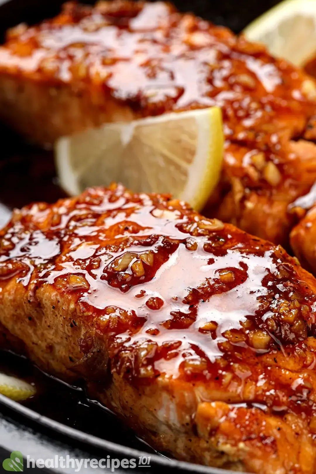A close-up picture of two honey garlic salmon fillets garnished with two slices of lemon