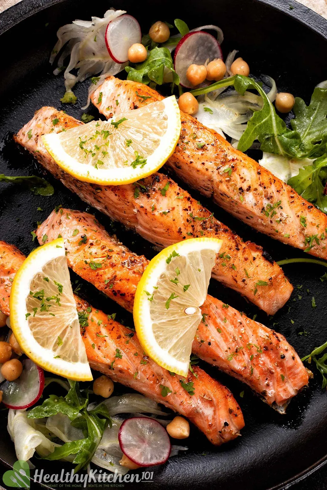 four salmon fillet in a cast iron skillet, top by lemon slices, chopped parsley