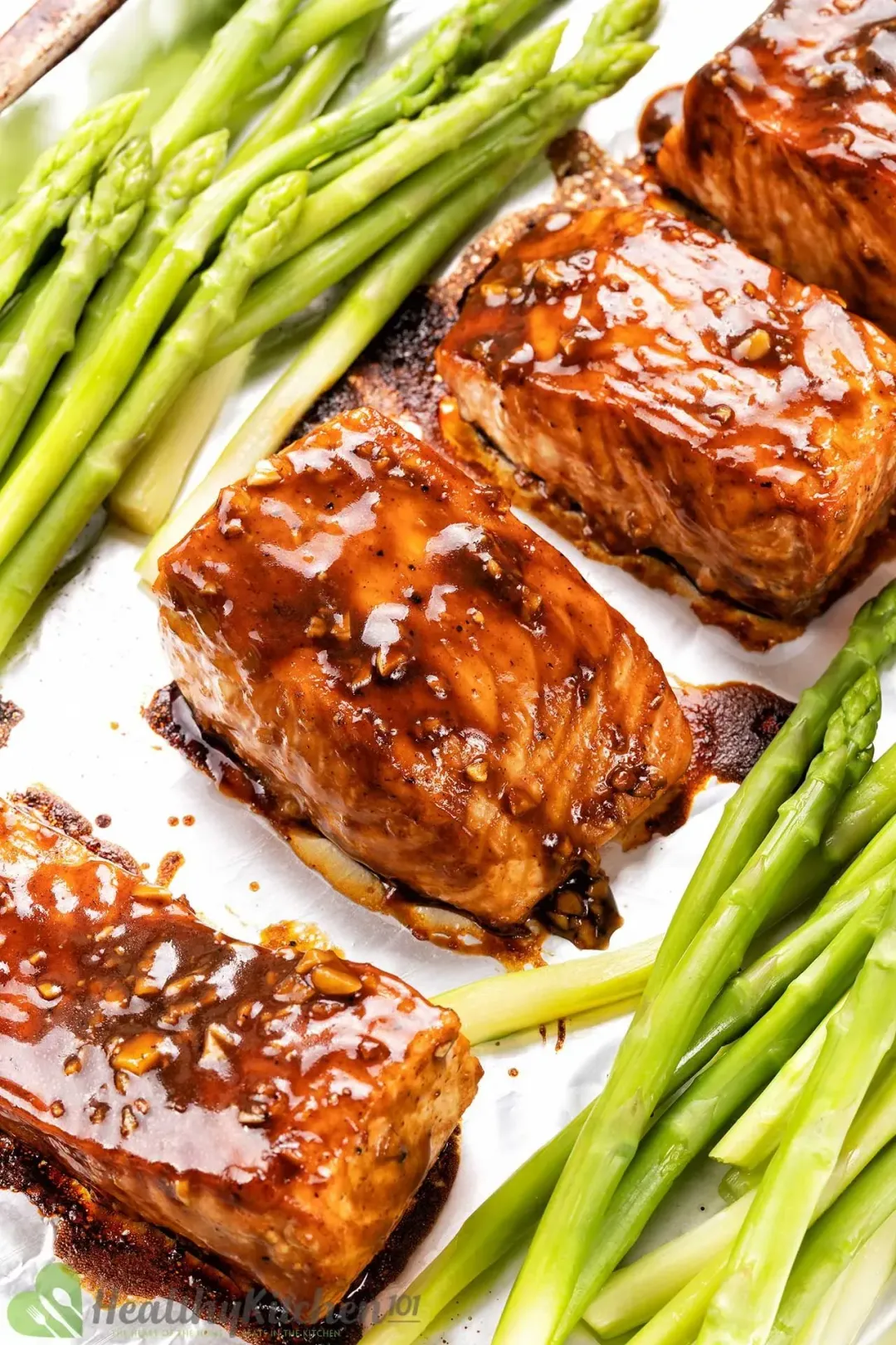 Four filets of salmon are fully coated in teriyaki sauce and placed on a baking sheet together with asparagus.