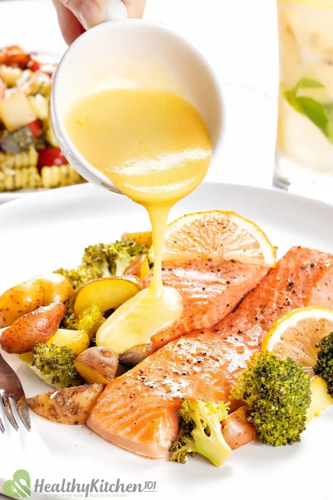 A yellow buttery sauce is being poured on a baked salmon filet served on a plate filled with baked potato and broccoli pieces.