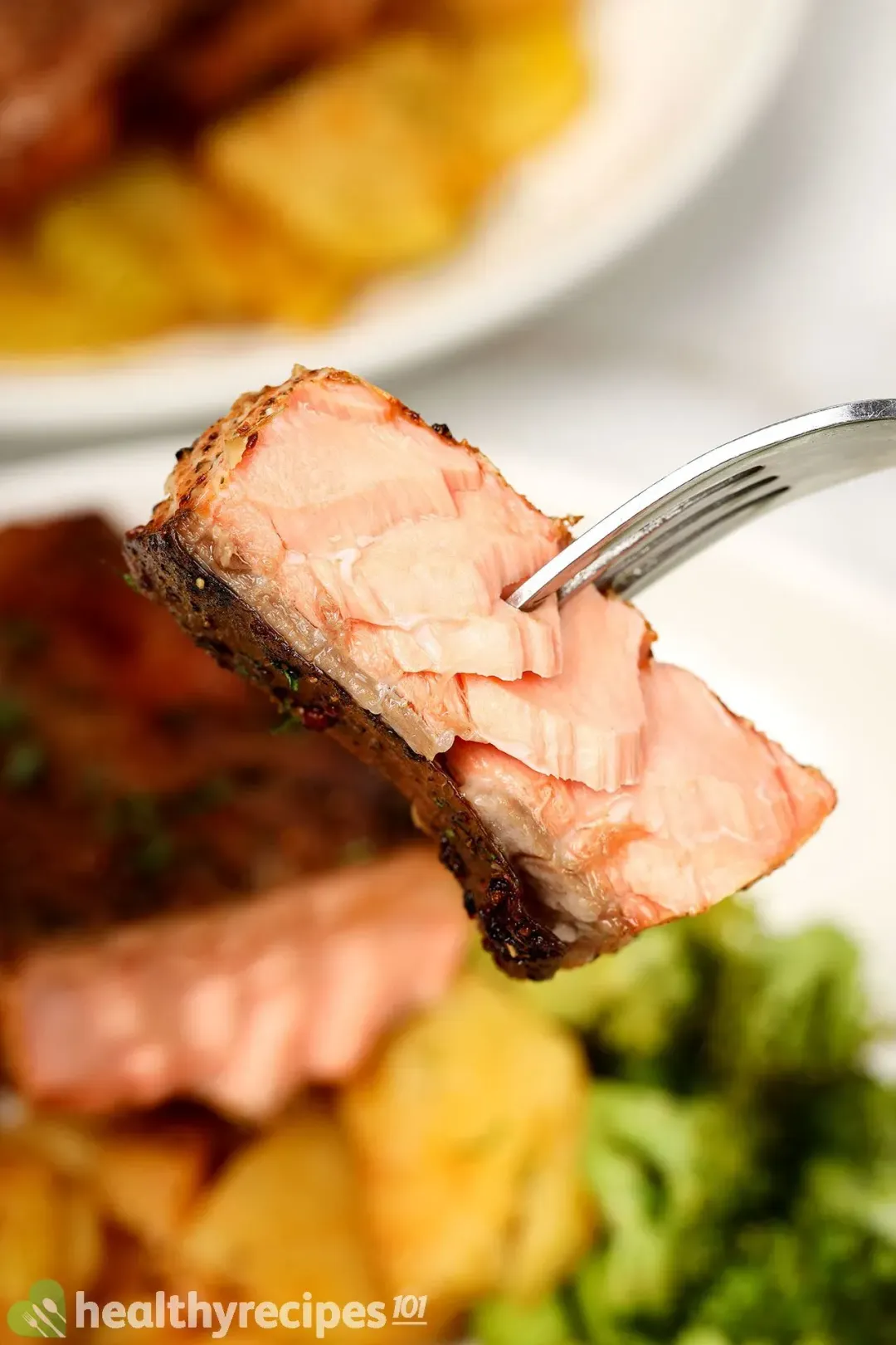 A fork piercing through a well-cooked piece of salmon whose meat is light pink and the skin is charred brown
