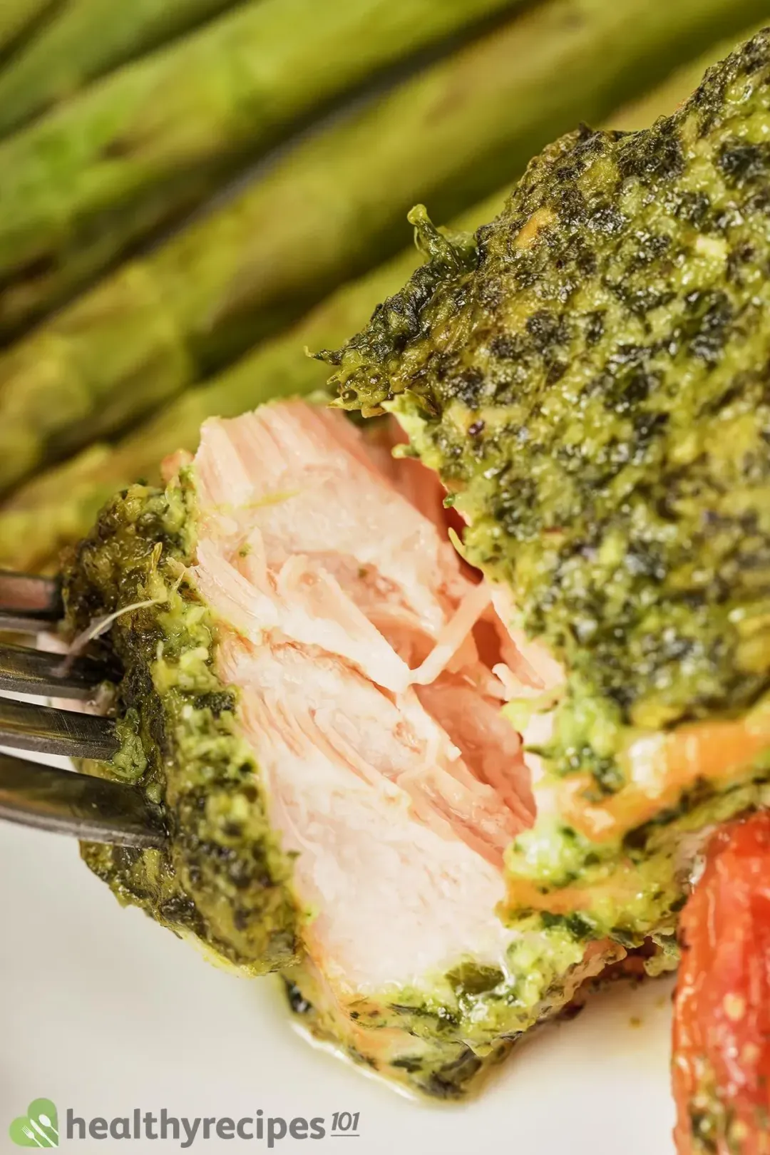 A close-up shot of a pesto salmon fillet with some baked asparagus and cherry tomatoes on the side