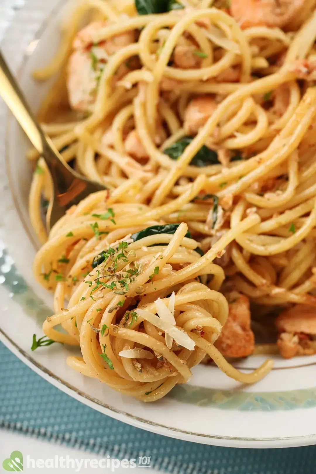 A close-up shot of a fork with spaghetti wrapped around it laid on the edge of a plate of salmon spaghetti