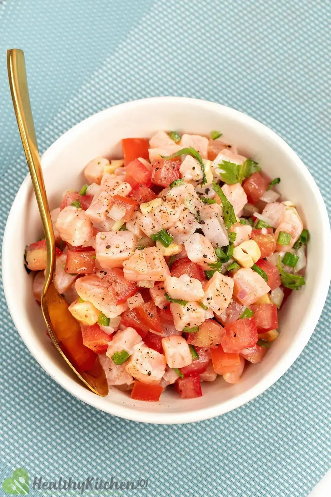 A small bowl of Lomi Lomi salmon with a golden spoon above a blue kitchen cloth