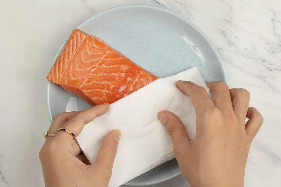 hand holds a kitchen towel to pat the salmon fillet dry