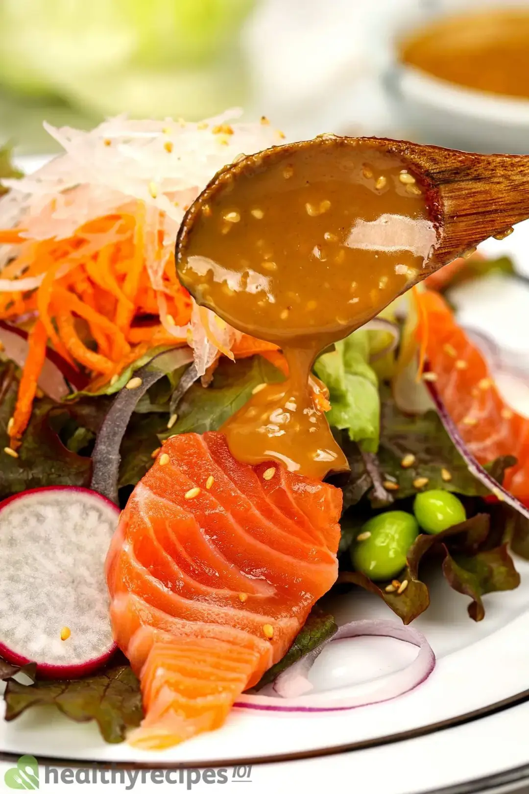 A close-up shot a wooden spoon drizzling sesame dressing on top of Japanese salmon salad