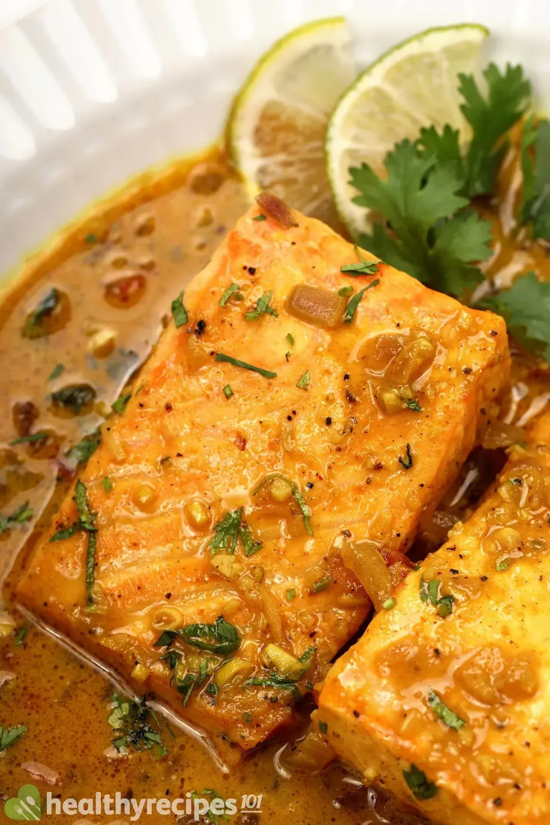 A close-up shot of cooked salmon fillets covered in chopped herbs next to a few lime slices and fresh coriander