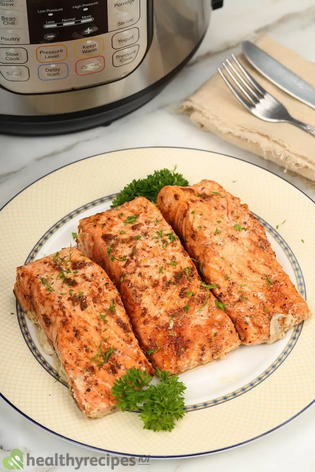 Three pieces of cooked salmon fillets on a platter with an Instant Pot and some dining utensils on the side