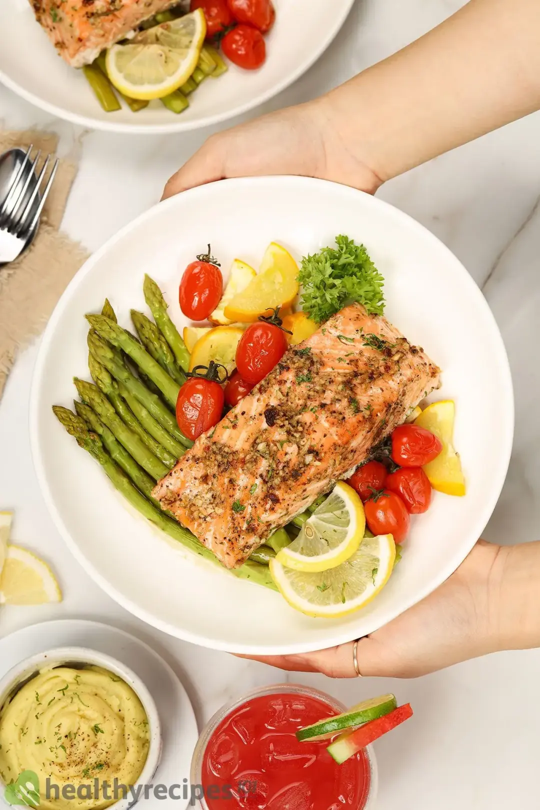 A piece of baked salmon fillet on a bed of vegetables including asparagus, cherry tomatoes, zucchini slices, and slices of lemon