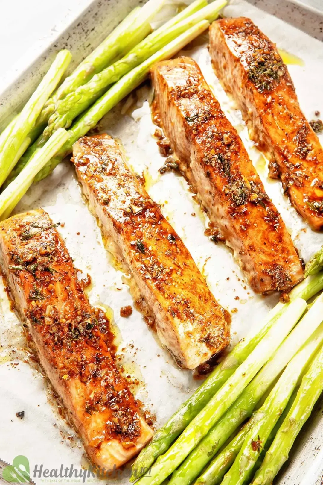 top view of four broiled salmon fillet side by side and asparagus on baking tray