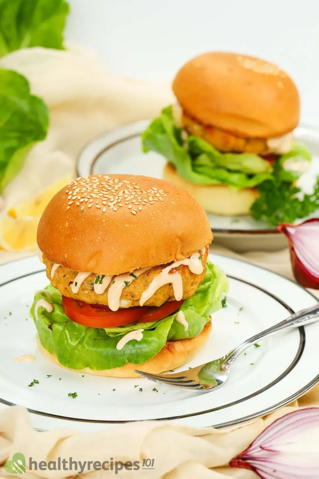 A burger and a fork placed on a plate with another similar plate of burger in the background