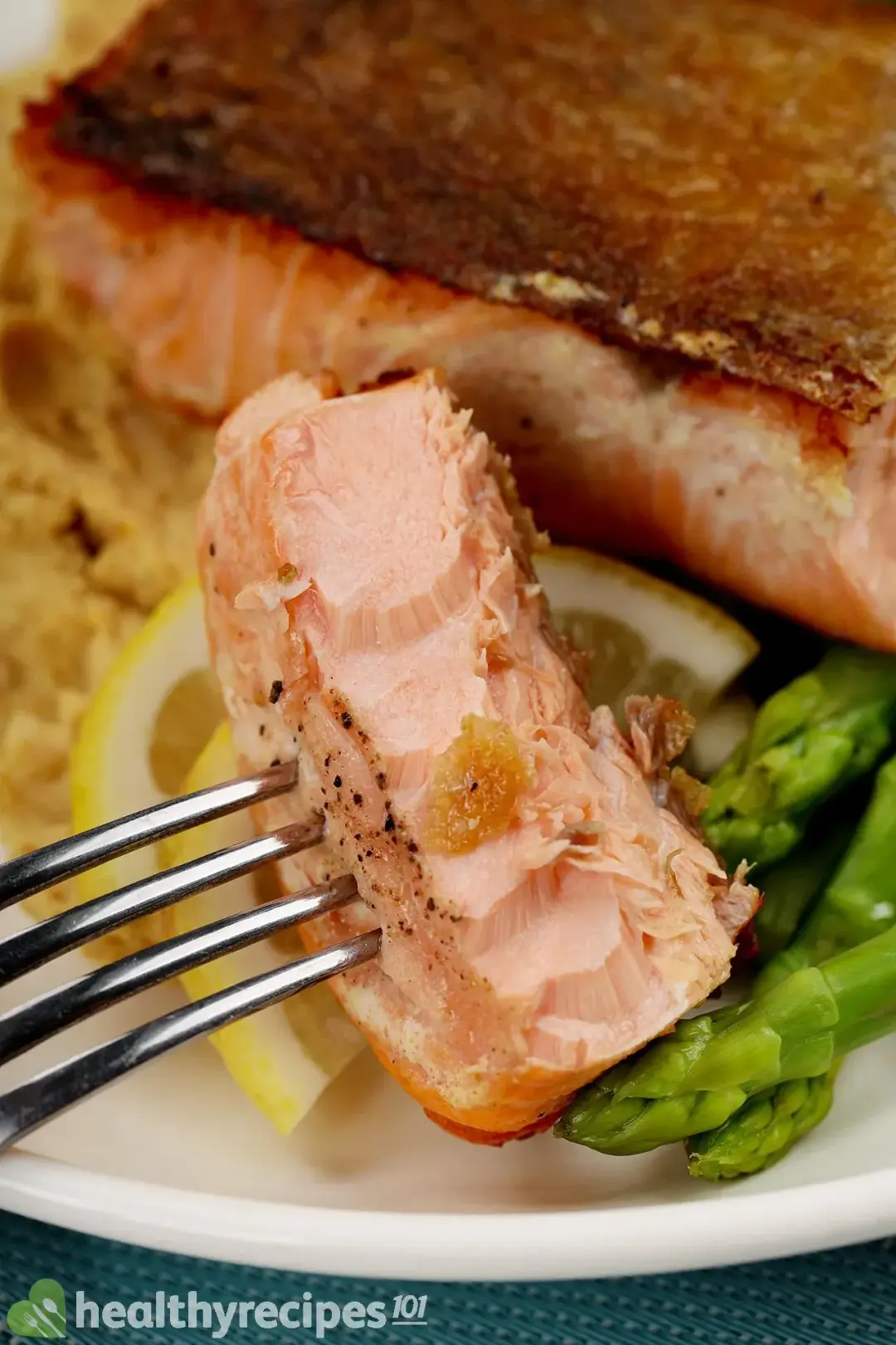 A plate of crispy-skin salmon served with mashed chickpeas, boiled asparagus, and two slices of lemon