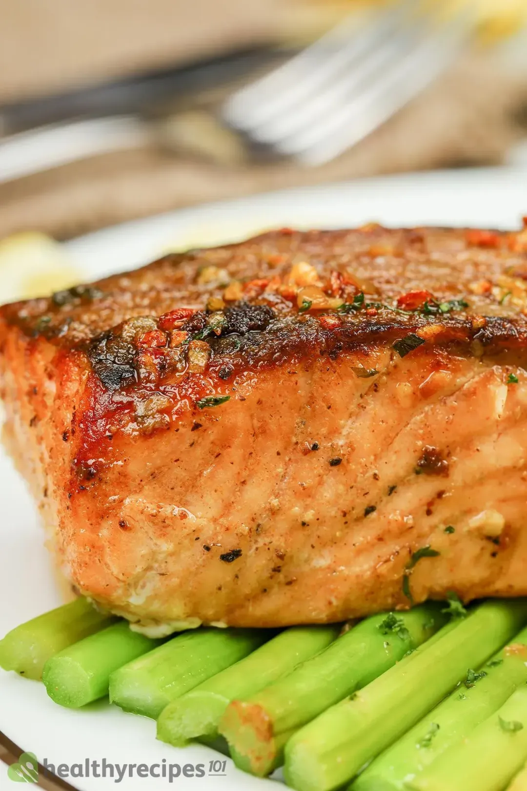 A close-up shot of a pan-seared salmon fillet with charred edges and pale orange meat laid on top of asparagus stalks
