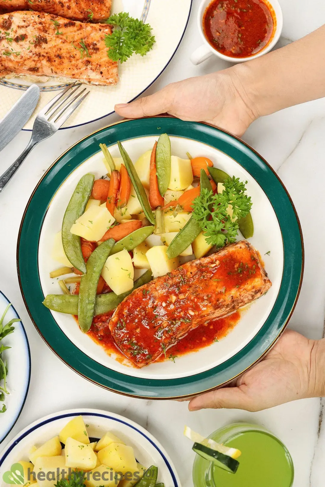 A plate of Instant Pot salmon surrounded by a glass of juice, a dipping sauce, and a plate of salad