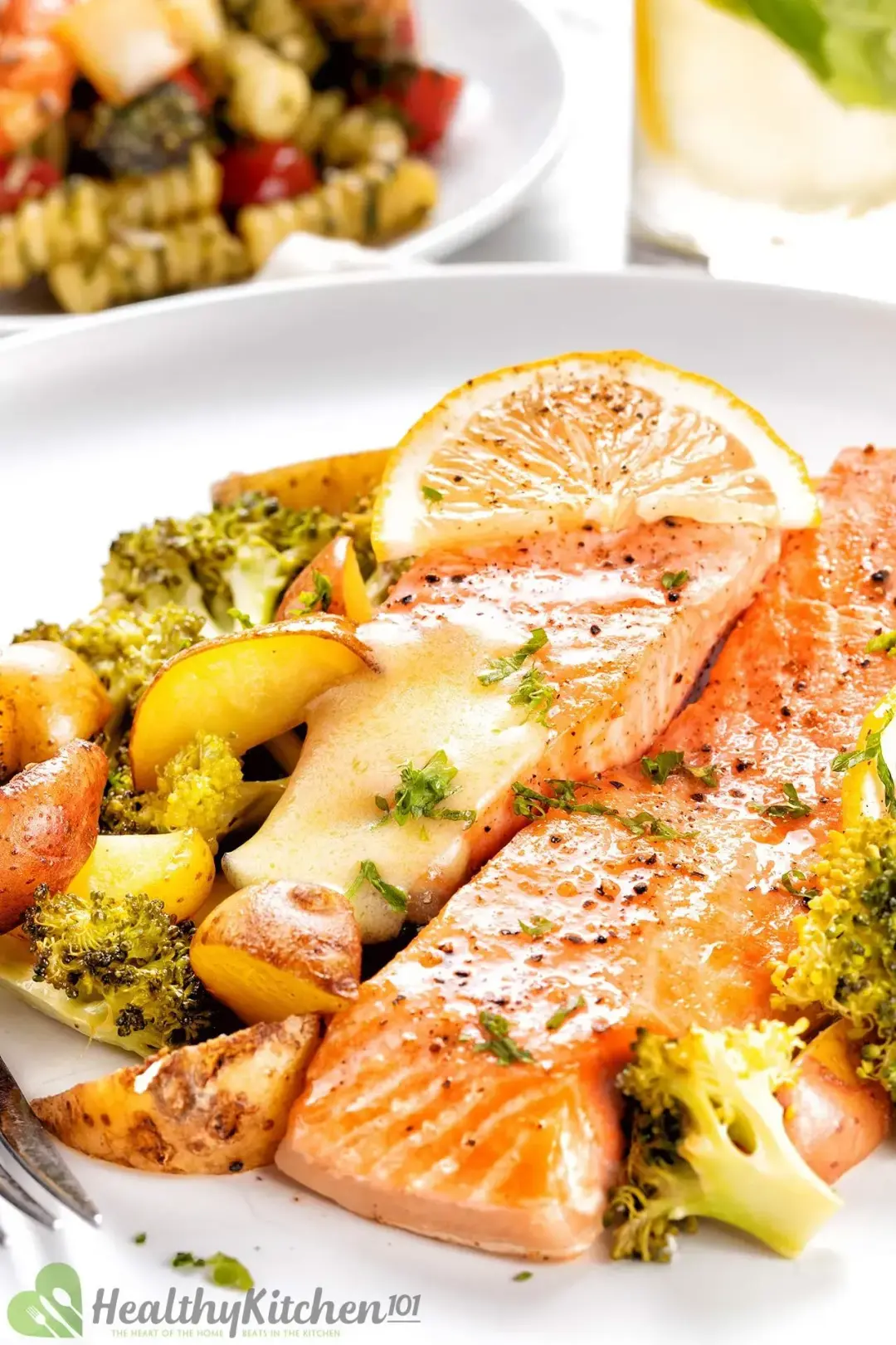 A serving plate of baked salmon, potato wedges, and broccoli, topped with a lemon slice.