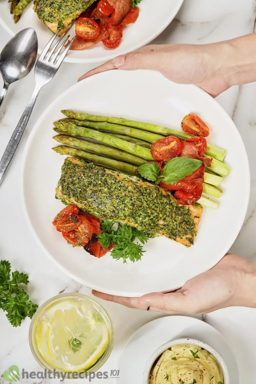 A plate of salmon pesto with a glass of lemonade and a bowl of mashed potatoes on the side